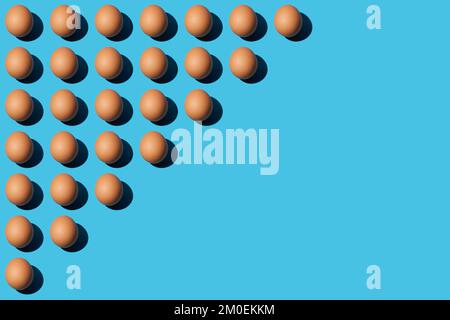 A pattern of brown chicken eggs lying diagonally on the upper left half of the blue background. Right side for copy space, close-up, top view. Stock Photo