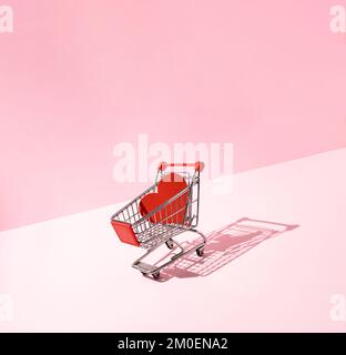 Red heart in shopping cart on pink background. Creative love or Valentines minimal concept. Stock Photo