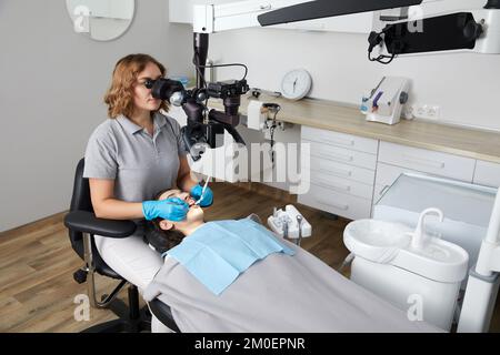 Female dentist with dental tools and microscope treating patient teeth at dental clinic office. Medicine, dentistry and health care concept. Stock Photo