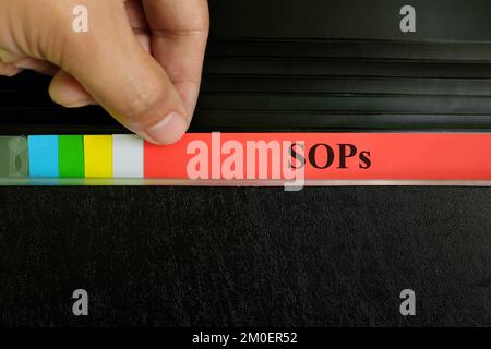 Hand picking SOP file record in black binder folder. Standard operating procedure concept. Stock Photo