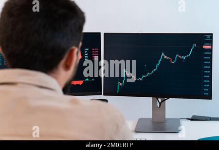 Young caucasian male finance broker analyzing stock graphs while trading from modern home office. Stock Photo