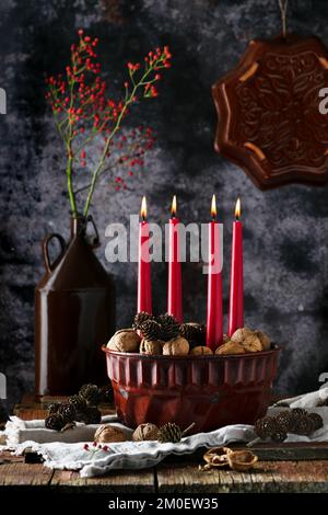 Beautiful Christmas floristic arrangement. Advent wreath with four red burning candles, walnuts and larch cones in an enamel bundt cake pan. Stock Photo