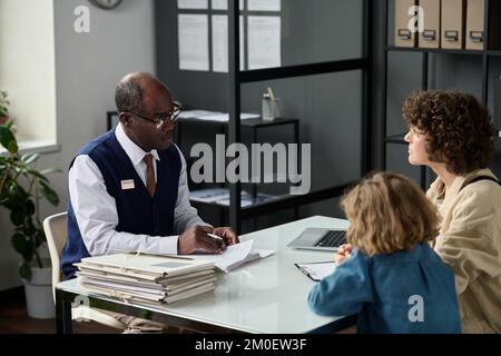 Portrait of senior black man consulting mother with child in insurance agency office Stock Photo