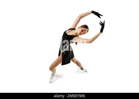 Studio shot of beautiful female figure skater in black festive stage dress practicing base elements of short program. Winter sports, flexibility Stock Photo