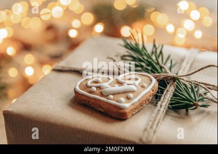 Close-up photo of heart shaped gingerbread cookie on christmas present in front of bokeh lights. Christmas present wrapped in brown paper and decorate Stock Photo