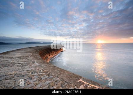 Lyme Regis, Dorset, UK. 6th Dec, 2022. UK Weather: Glorious winter sunrise over the iconic Cobb at the coastal resort of Lyme Regis. The rising sun lights up the wintery sky on a chilly December morning. Credit: Celia McMahon/Alamy Live News Stock Photo