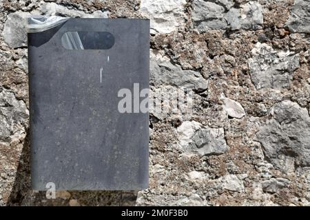 Horizontal photo of grey metal trash can on left side with stone wall in background. Rectangular container for rubbish hanging on fortress wall Stock Photo