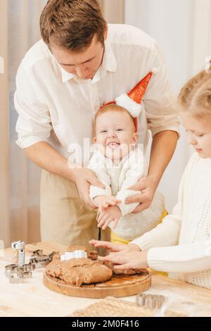 Dad makes gingerbread cookies in the kitchen with his little daughter wearing a santa hat Stock Photo