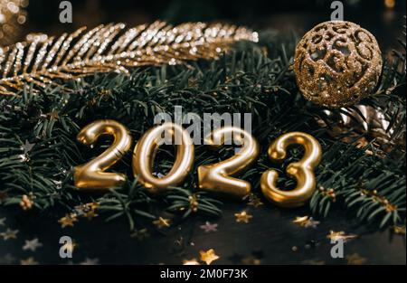 Close-up still life photo of golden numbers and decorations for new year 2023. Gold bauble and decorations on dark green pine branch. Stock Photo