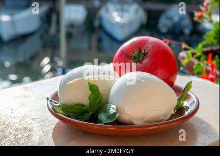 White soft italian mozzarella bufala cheese in balls with red tomato and basil served outdoor Stock Photo