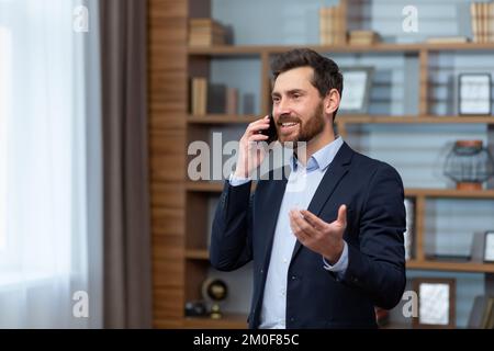 Mature businessman boss talking on phone smiling and happy, senior man in business suit working inside classic office. Stock Photo