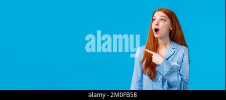 Omg check it out. Startled and emotional impressed redhead female drop jaw, staring upper left corner with amazed expression, popping eyes at Stock Photo