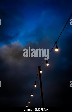 A row of light bulbs held up by wooden post against a very dark and eerie blue sky.Plenty of room for copy.A haunting and atmospheric image. Stock Photo