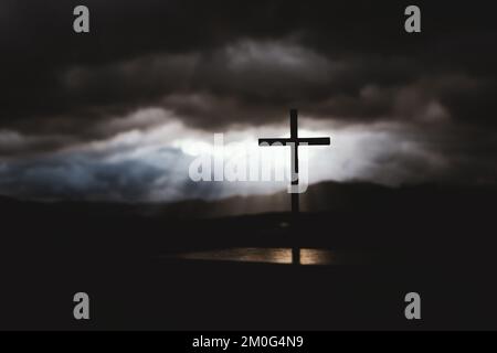 A beam of light shining through a bright sky and flowing clouds, and a silhouette of the holy cross symbolizing the suffering, death, and resurrection Stock Photo