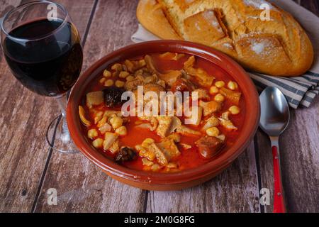 clay casserole with Madrid-style stewed tripe, typical spanish food on a wooden table with a brick wall in the background. Stock Photo