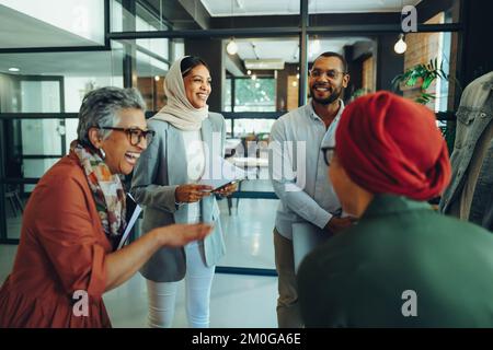Group of happy business colleagues laughing cheerfully during a staff meeting in a modern office. Successful businesspeople working as a team in a mul Stock Photo