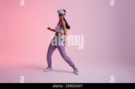 Happy young woman dancing in the metaverse. Active young woman laughing cheerfully while wearing virtual reality goggles. Woman having fun while explo Stock Photo