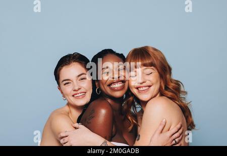 Group of happy women with different skin tones smiling and embracing each other. Three diverse women feeling comfortable in their natural skin. Body p Stock Photo