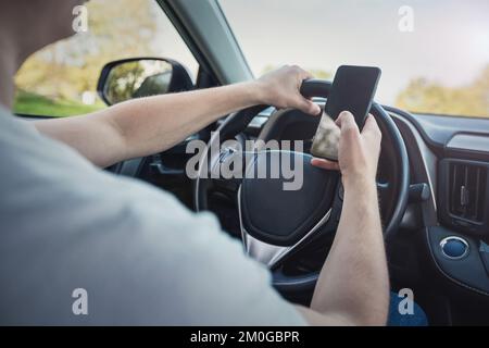 Young driver guy distracted by his phone while in front of the steering wheel, using his smartphone with one hand while driving. Risk and danger situa Stock Photo