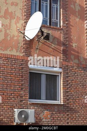 Satellite dish and air conditioner on the wall of an old apartment building Stock Photo