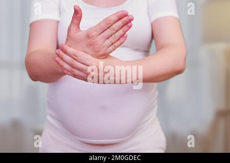 A pregnant woman holds her hand. Tunnel syndrome in the wrist during pregnancy. Stock Photo