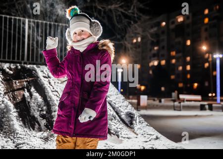 A little girl is very happy with the first snow on a cold winter night. Stock Photo