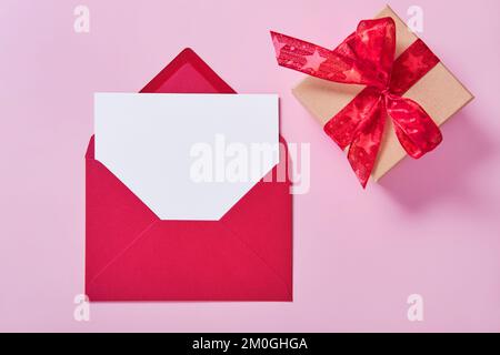 Greeting card mockup, white blank card in envelope and gift box on pink background. Stock Photo