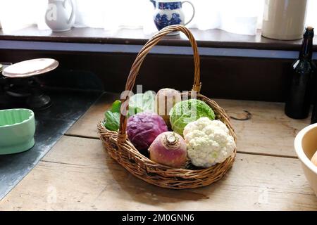 Freshly cut vegetables in a wicker basket on an old fashioned work surface - John Gollop Stock Photo
