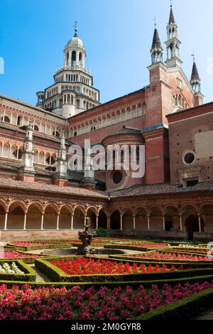 Inner courtyard decorated with planted flowers behind cloister, large 15th century cathedral behind, Charterhouse of Pavia, Certosa di Pavia, Lombardy Stock Photo