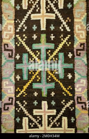 Handmade beige black carpet with geometric ornament, braided mat. Knitted bath mat or toilet mat, close-up, texture background. Full frame, top view Stock Photo