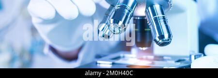 Biological scientist looking at  samples by using microscope doing research for new vaccine in pharmaceutical labolatory Stock Photo