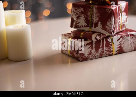 photo wrapped gifts in red paper on a gray table with blurry lights in the background Stock Photo
