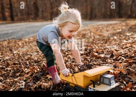 Happy child playing in fall leaves with toy truck Stock Photo