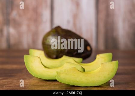 Avocado chunks on a rustic wooden table, with an avocado in the background out of focus. Stock Photo