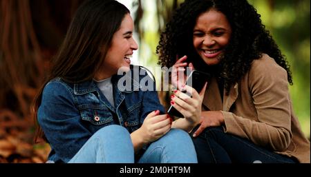 Happy friends hugging and embracing while looking at cellphone Stock Photo