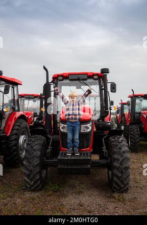 Presentation and sale of new red tractors standing in a row. The child happily stands on a farm tractor. Equipment for farming and agribusiness. The b Stock Photo