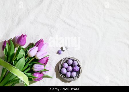 Easter corner composition with bunch of pink magenta tulips and nest, wreath with quail Easter eggs. Flat lay on off white textile tablecloth Stock Photo