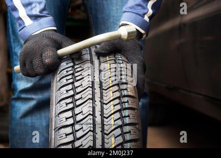Closeup of mechanic hands holding a tire and wrench at the repair garage Stock Photo