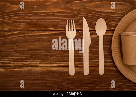 Wooden fork, spoon, knife and cardboard plate and cup on wooden background Stock Photo