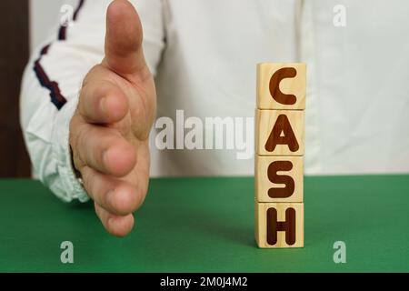 Business concept. On a green surface, cubes with the inscription - CASH. The man holds out his hand. Stock Photo