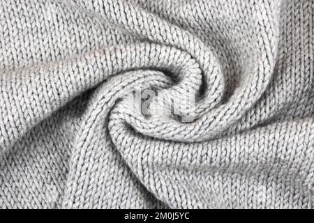 Knitted gray background. Close-up of a knitted blanket. Wavy folds material. Knitted warm grey sweater or scarf. Stock Photo