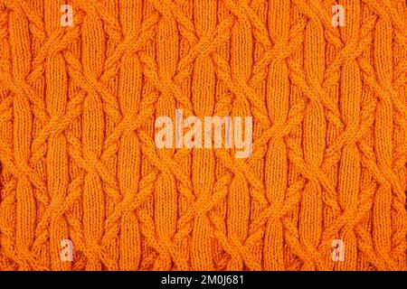 Knitted orange background. Large knitted fabric with a pattern. Close-up of a knitted blanket. Stock Photo