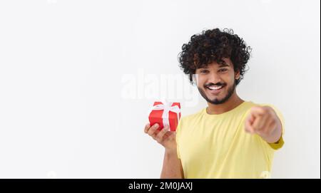Happy young Asian man with curly hair hold red gift box toothy smile looking at camera on white background Stock Photo