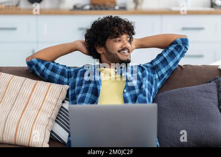 Happy smiling Asian man freelancer with laptop resting with hands behind head distracted from online work Stock Photo