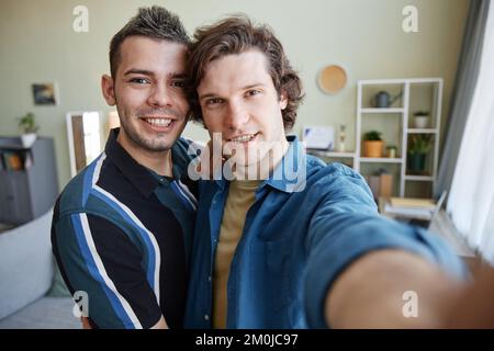 Portrait of young gay couple taking selfie photo in new home together, camera POV Stock Photo