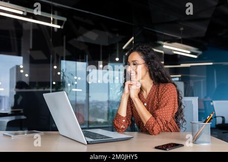 Happy and smiling hispanic businesswoman typing on laptop, office worker with curly hair and glasses happy with achievement results, at work inside office building. Stock Photo