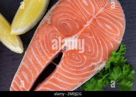 Raw salmon steak top view with lemon and parsley on dark background. Stock Photo