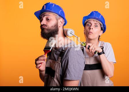 Team of painters using paintbrush and roller in studio, working on painting job with tools. Construction workers experts wearing overalls and posing with brushes, doing renovation project work. Stock Photo