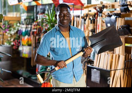Smiling african american gardener buying shovel in gardening market Stock Photo