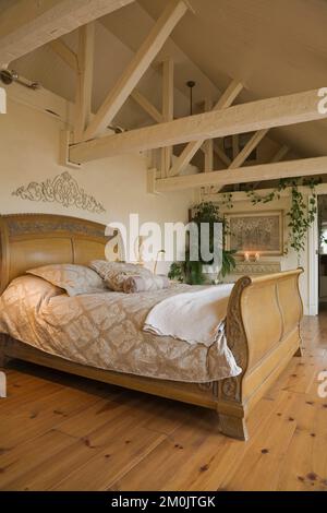 Luxurious antique wooden sleigh bed and furnishings in master bedroom with pinewood floorboards in attic inside old circa 1840 cottage style home. Stock Photo